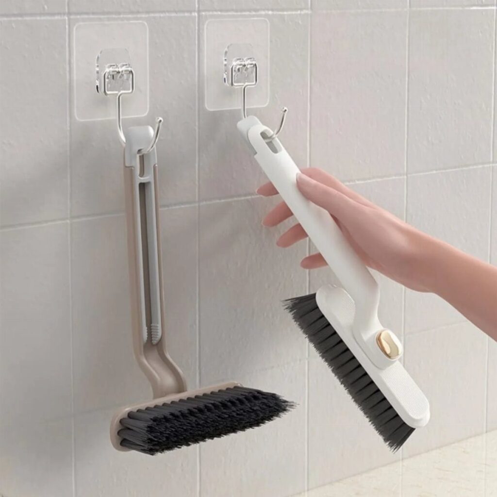 A hand holding a white scrub brush with black bristles against white wall tiles.