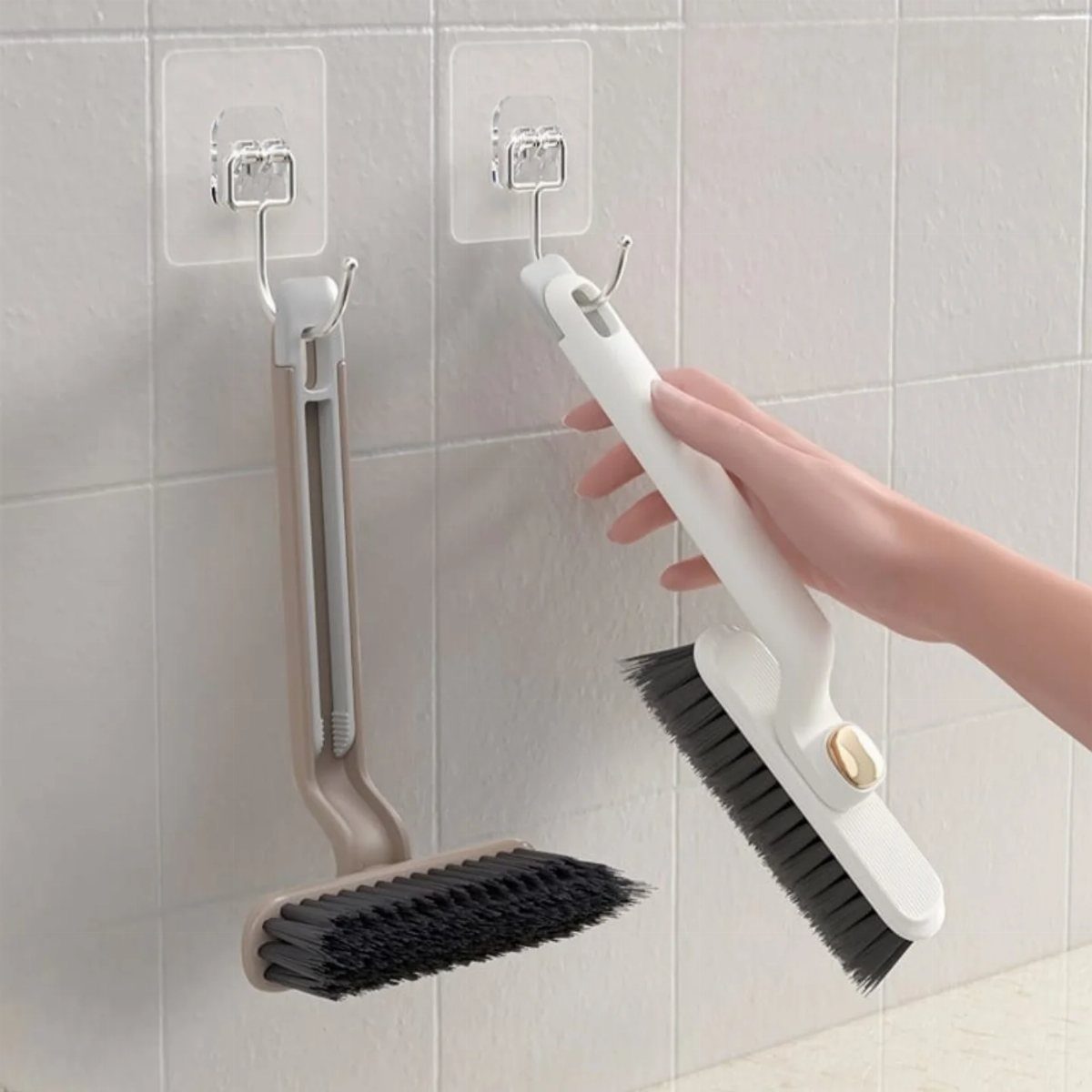 A hand holding a white scrub brush with black bristles against white wall tiles.