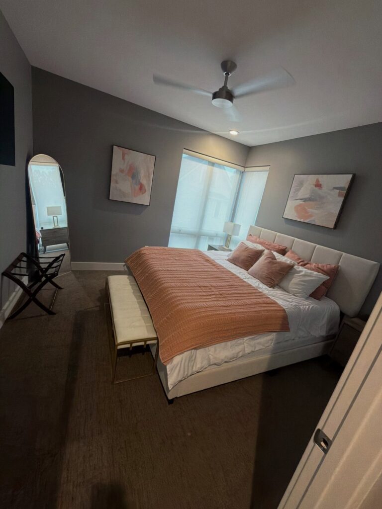 A modern bedroom featuring a large bed with pink bedding and grey walls.