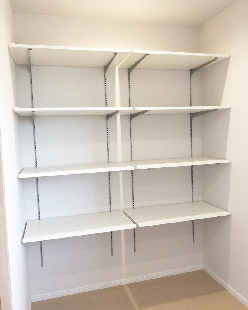 White adjustable shelves mounted on metal tracks inside a clean, white pantry or closet space.