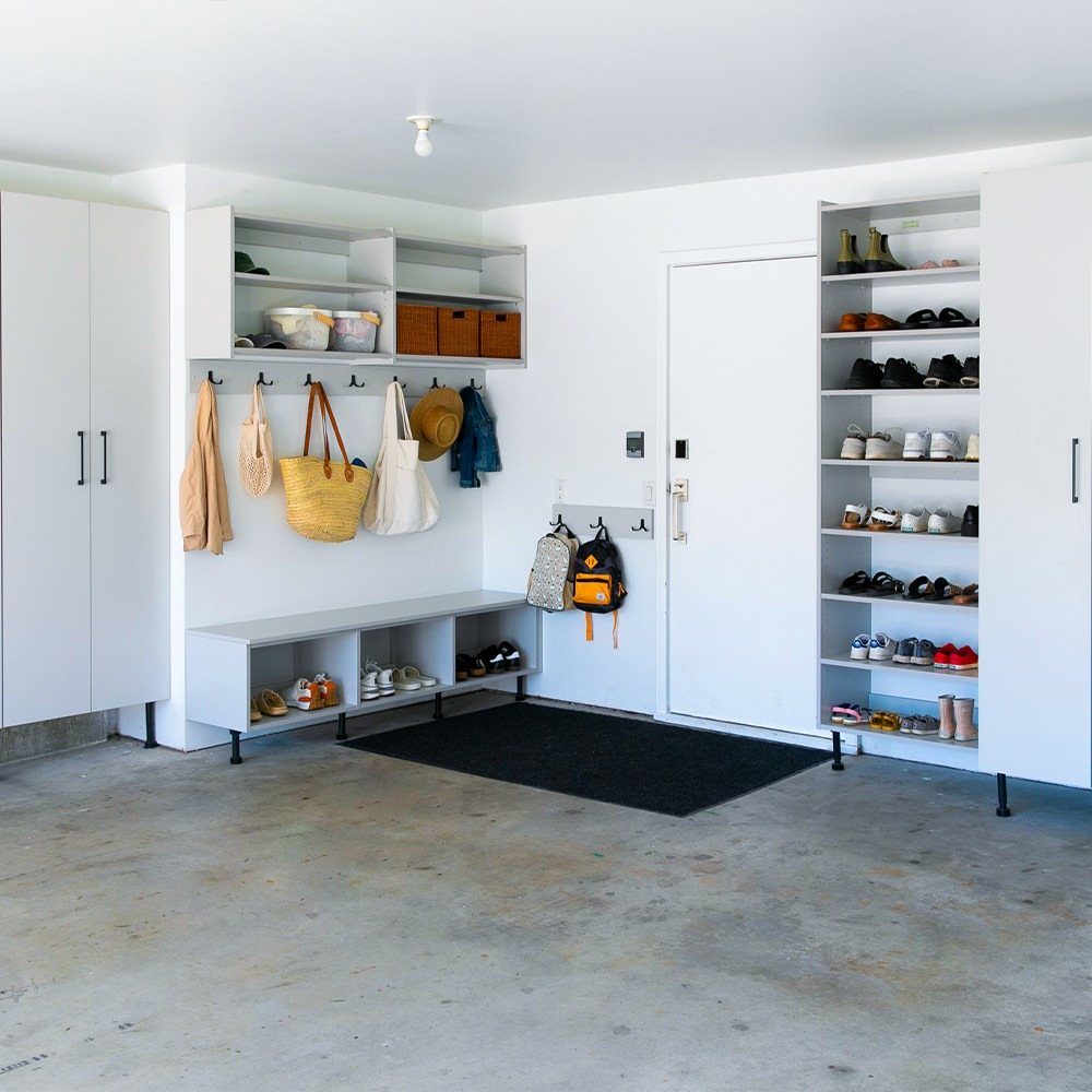 Organized white garage storage system with cubbies, hooks, and a tall shoe rack.