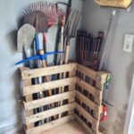 Wooden pallets used as vertical storage racks for garden tools in a corner.
