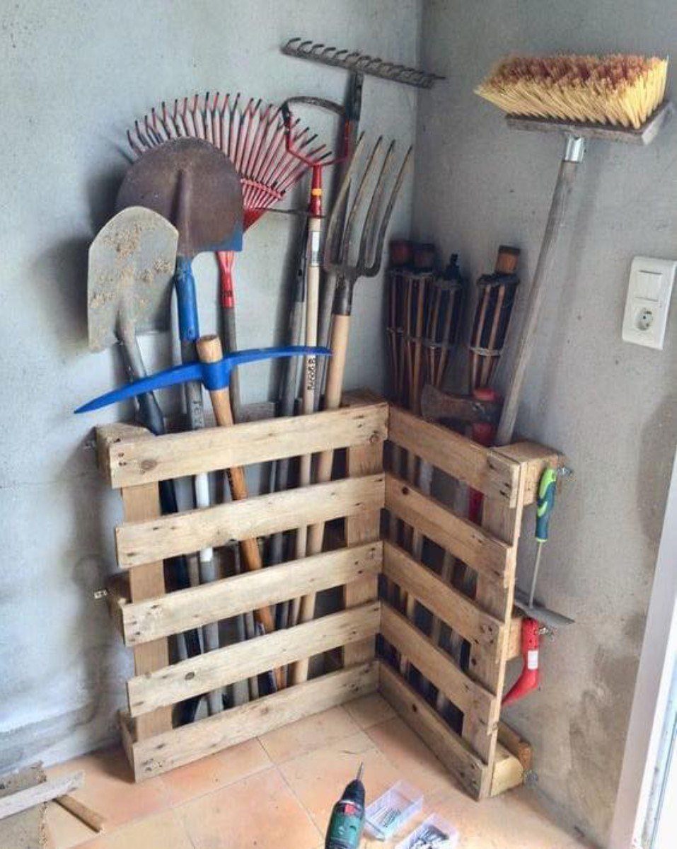 Wooden pallets used as vertical storage racks for garden tools in a corner.