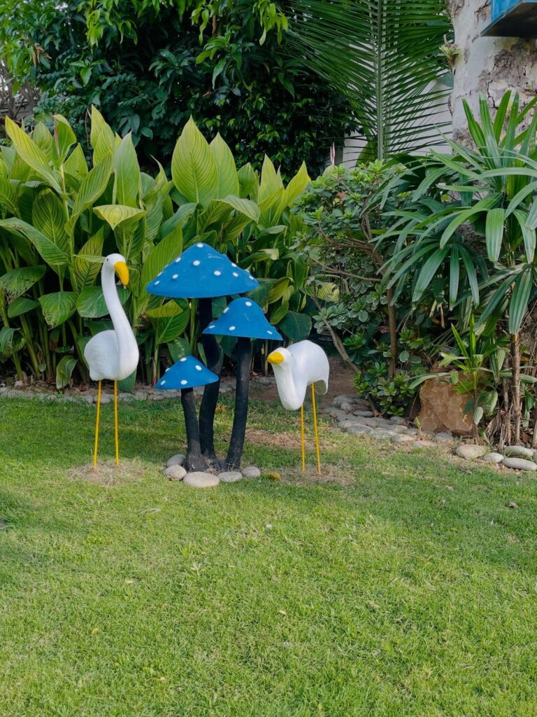 Blue mushroom sculptures and white bird statues standing on a green lawn surrounded by tropical plants.