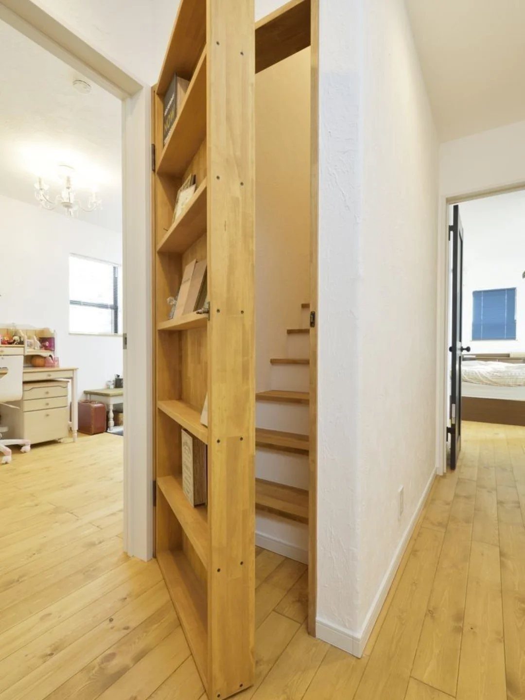 A wooden bookcase door swings open to reveal a hidden staircase in a bright hallway.