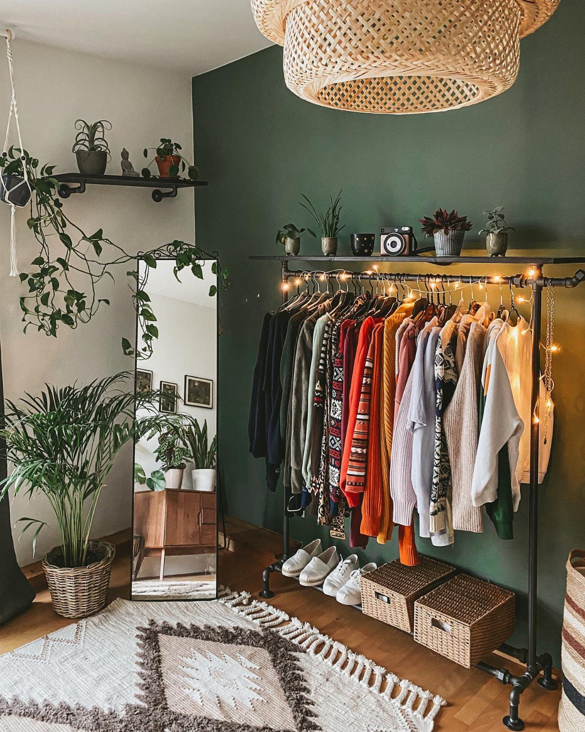 A black metal pipe clothing rack filled with colorful clothes against a green wall.