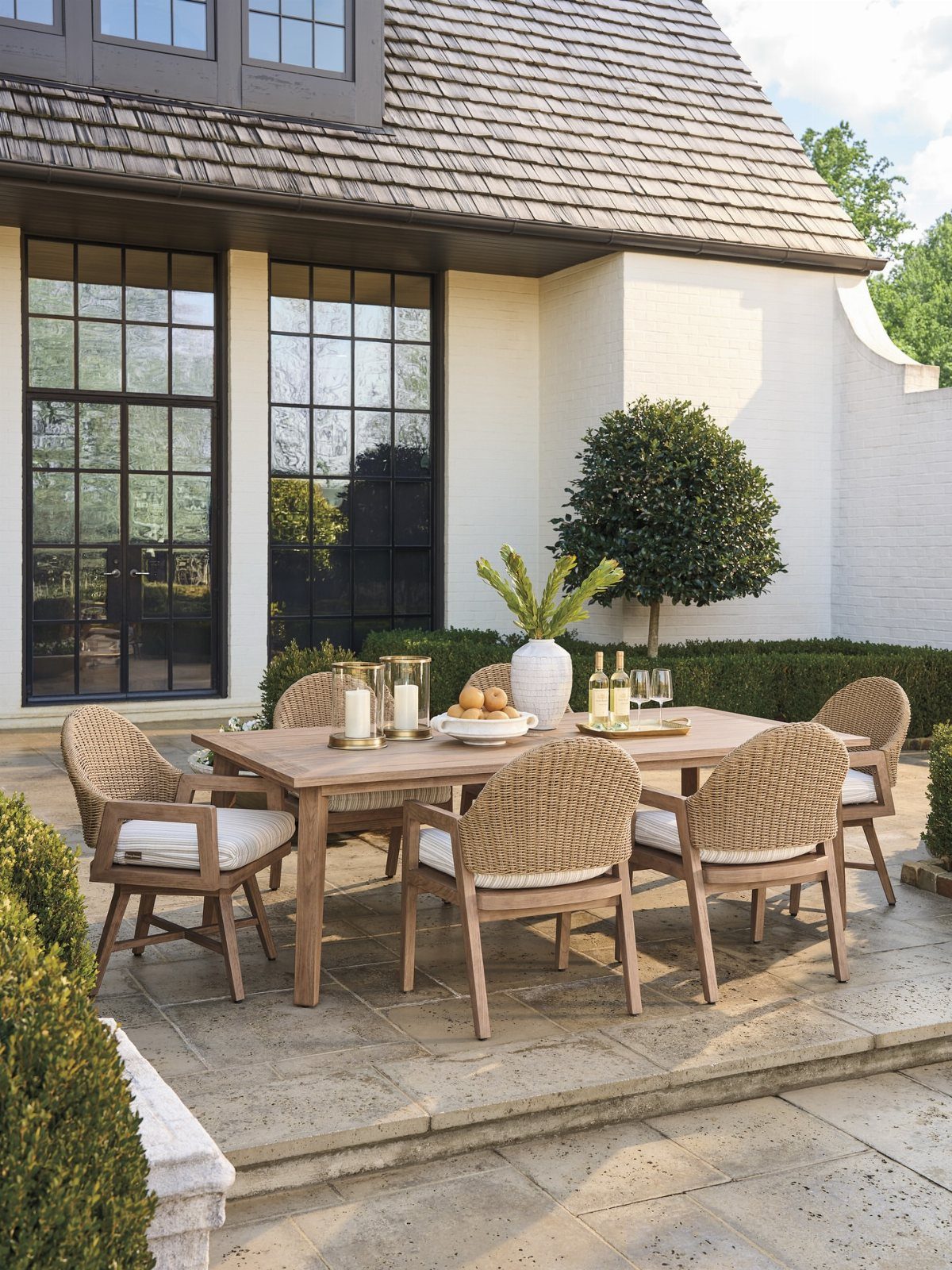 Wooden dining table with woven chairs and white cushions on a stone patio.