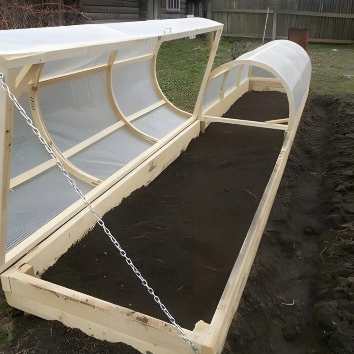 A wooden raised garden bed featuring a translucent arched plastic tunnel cover over dark soil.