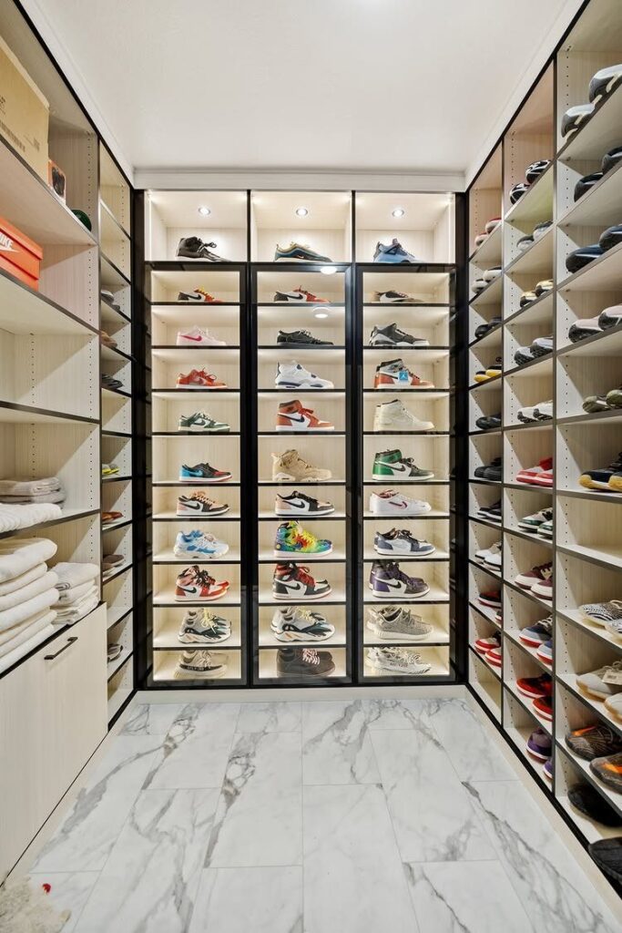A walk-in closet with white marble floors and shelves filled with many colorful sneakers.